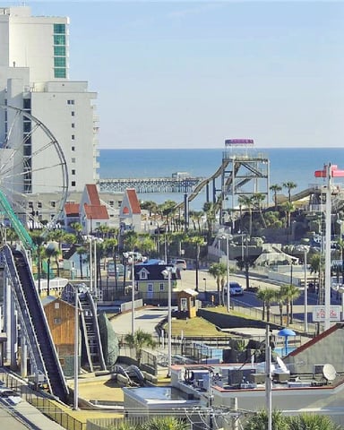 Beachfront boardwalk with Ferris wheel, roller coaster, and amusement park rides overlooking ocean and pier