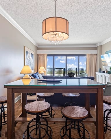 Open-plan living room with kitchen island, bar seating, ocean view balcony, and pendant lighting fixture