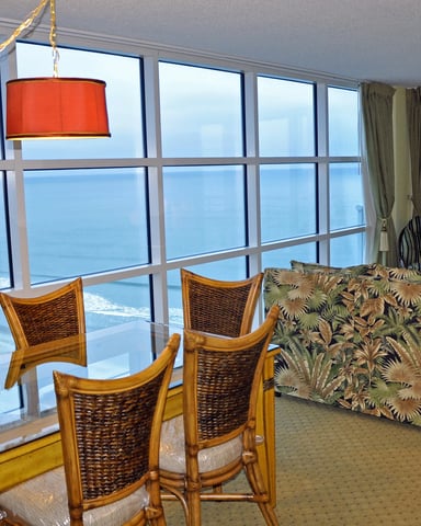 High-rise oceanfront living room with floor-to-ceiling windows, dining table, patterned sofa, and red pendant lamp.