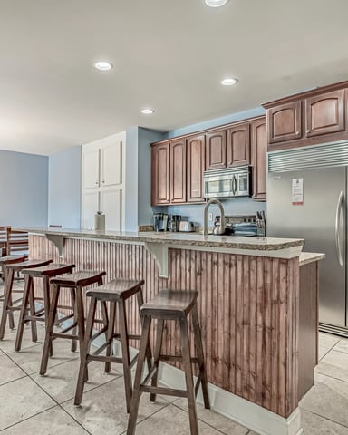 Open-plan kitchen and dining area with wood cabinetry, stainless steel appliances, island with bar seating, and beach-themed artwork.