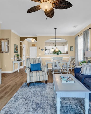 Open-plan living room with cream walls, dark blue sofa, striped armchair, and dining area visible through archway