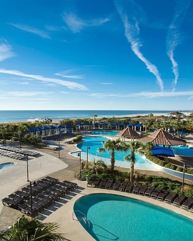 Aerial view of resort with multiple pools, water slides, palm trees, and ocean coastline under clear blue sky