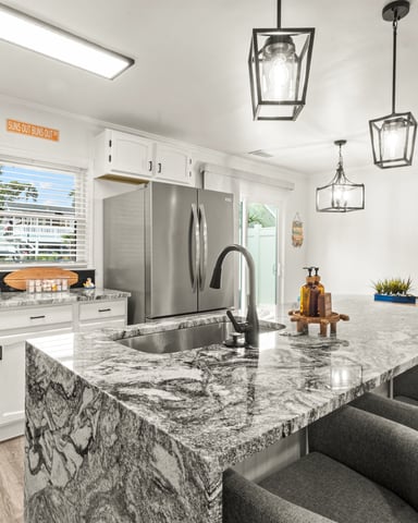 Modern kitchen with white cabinetry, granite countertops, stainless steel appliances, island seating, and pendant lighting