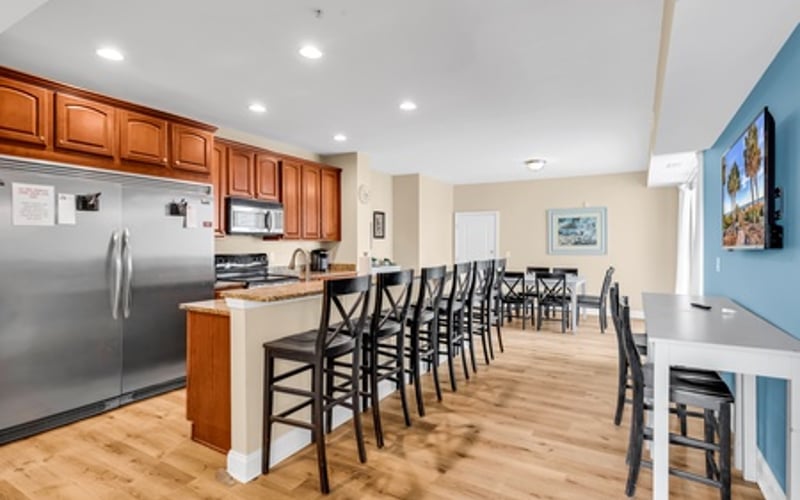 Open-plan kitchen and dining area with wood cabinetry, stainless steel appliances, island with black bar stools, and hardwood flooring