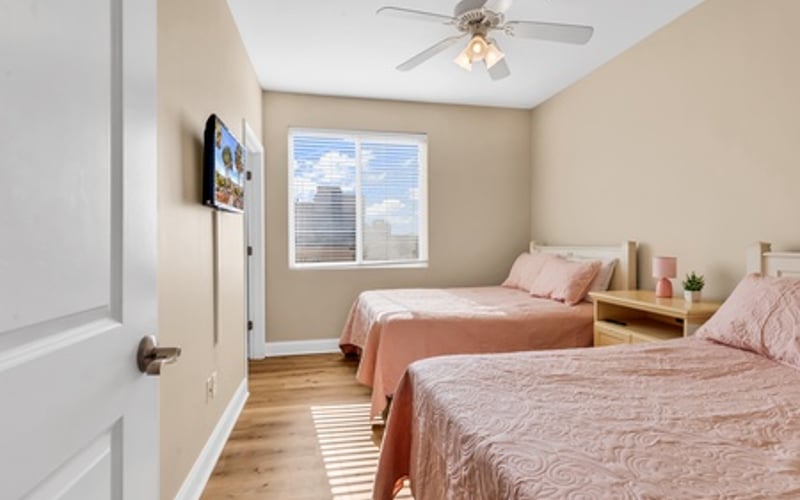 Bedroom with two twin beds, beige walls, ceiling fan, and window with blinds