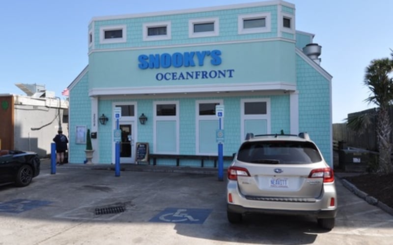 Light blue oceanfront restaurant building with white trim and parked car in front