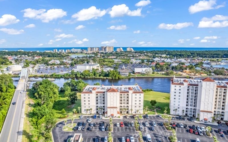 Aerial view of waterfront residential buildings with parking lot, canal, and distant coastal city skyline