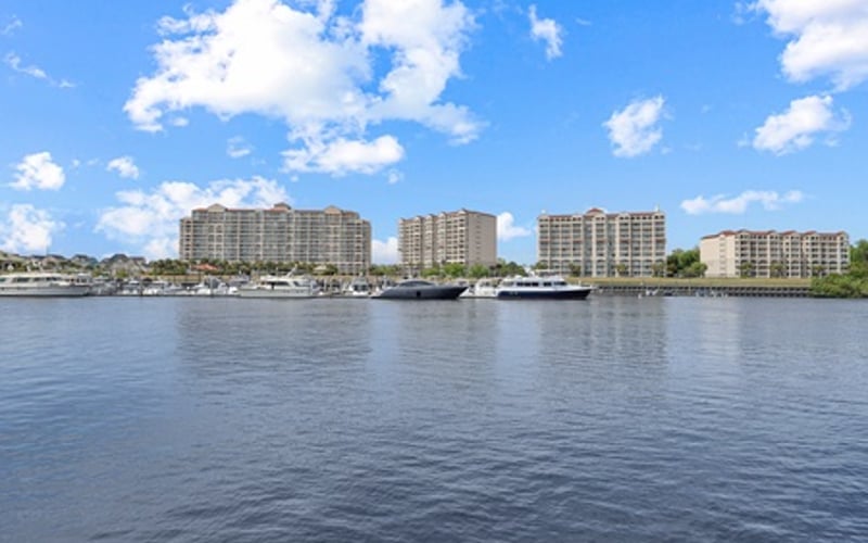 Waterfront view of multi-story residential buildings and docked boats along calm blue water under partly cloudy sky