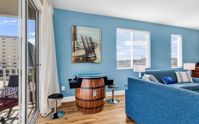 Bright living room with blue walls, blue sofa, wooden barrel side table, and balcony access with city views