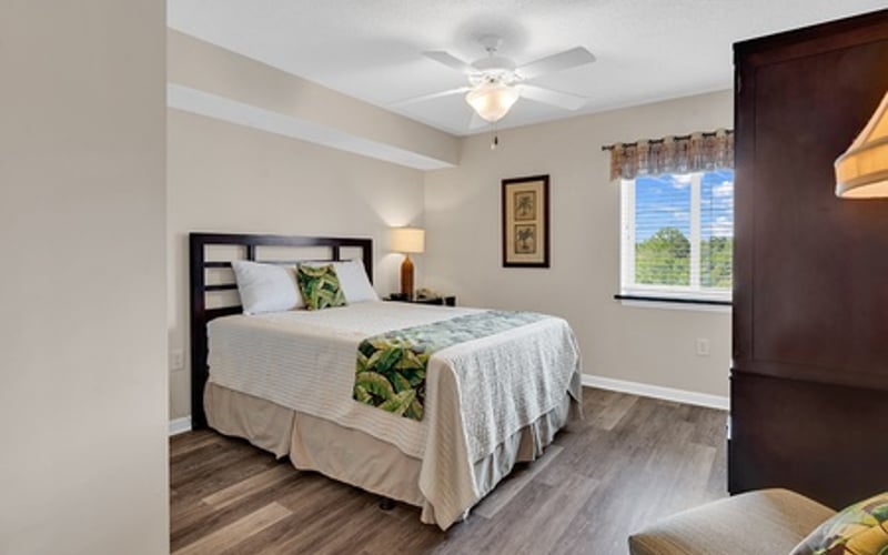 Bedroom with queen bed, dark wood headboard, ceiling fan, and window with natural light