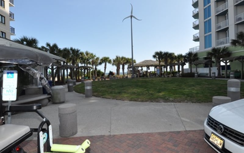 Beachfront plaza with palm trees, wind turbine, and residential high-rises on sunny day