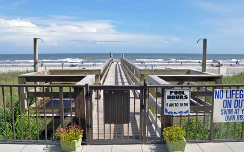 Wooden boardwalk gate leading to beach with ocean, pier, and lifeguard station visible beyond
