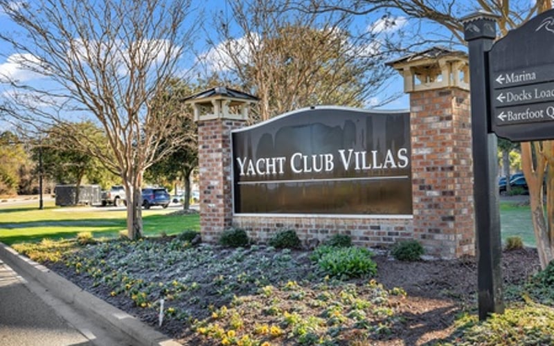Yacht Club Villas brick entrance sign with landscaping and bare trees under blue sky