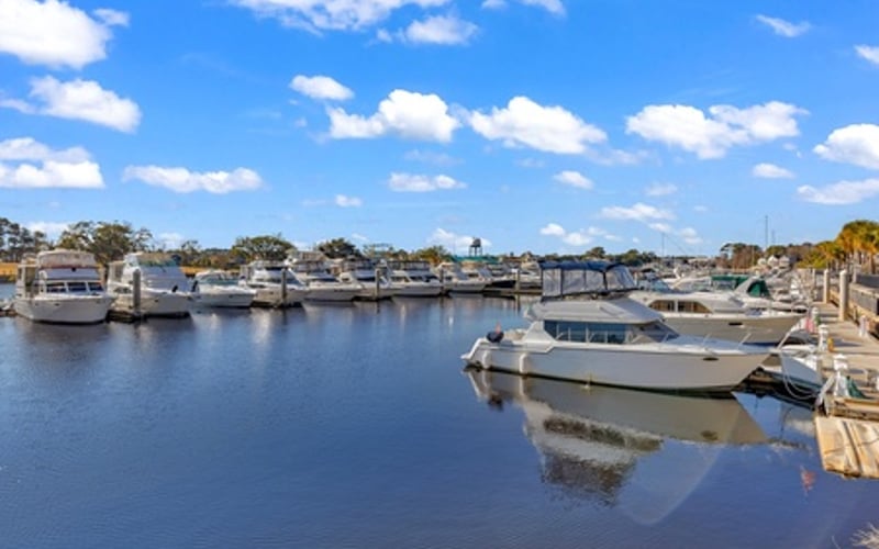 Marina with moored boats and calm blue water under clear sky with white clouds
