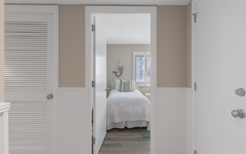 Hallway with open doorway leading to bedroom with white bedding and neutral walls