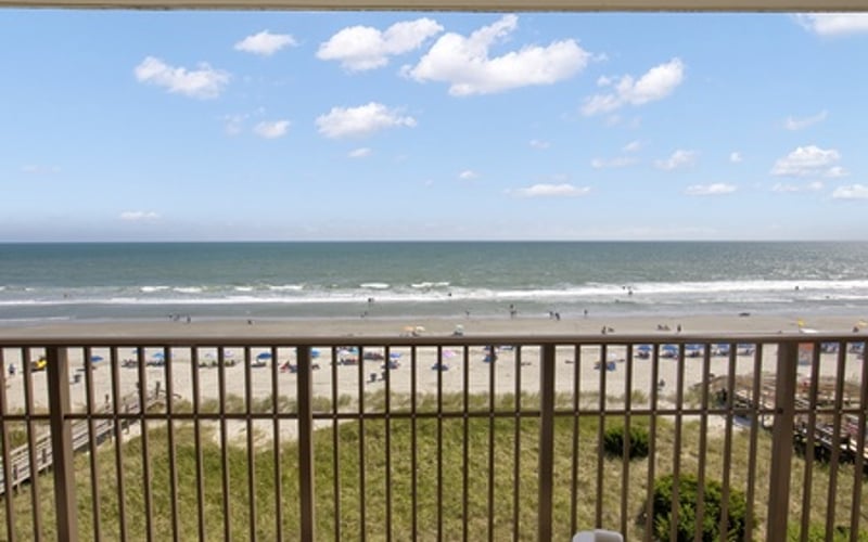 Oceanfront balcony with metal railing overlooking sandy beach and Atlantic Ocean with scattered clouds