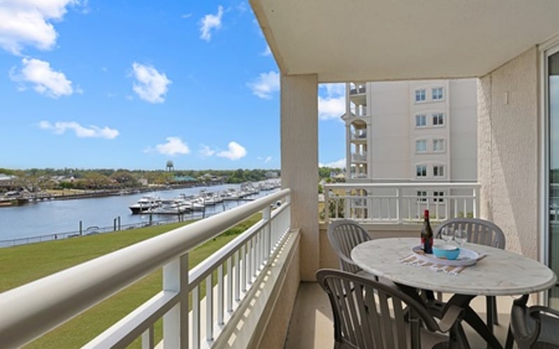 Waterfront balcony with dining table, overlooking marina and river under blue sky
