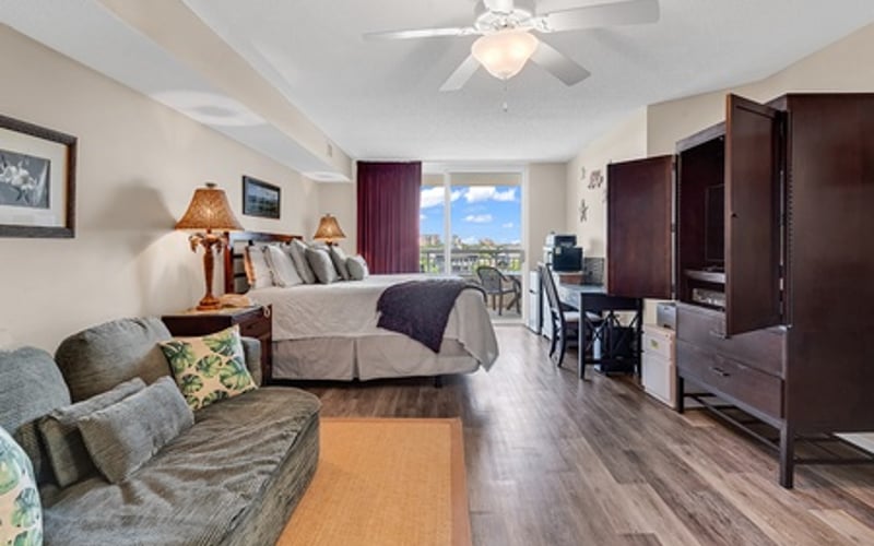 Studio apartment with bed, seating area, dark wood furniture, and city view through windows
