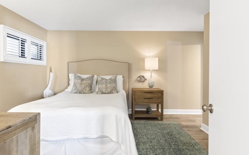 Bedroom with white bedding, arched headboard, wooden nightstand, and green runner rug