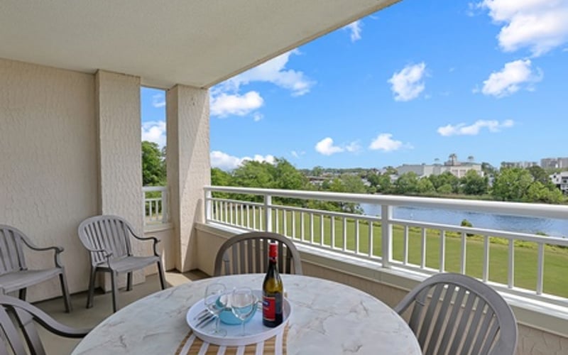 Waterfront balcony with dining table, lounge chairs, and river view under blue sky