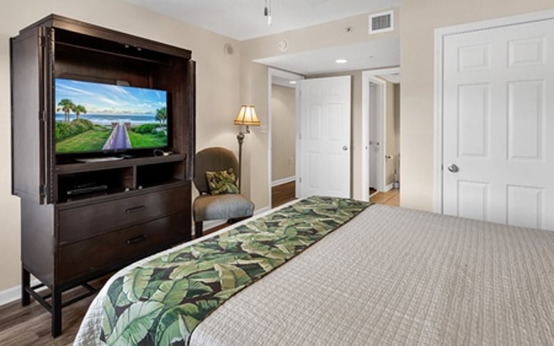 Bedroom with queen bed, dark wood TV cabinet, white doors, and beige carpet flooring
