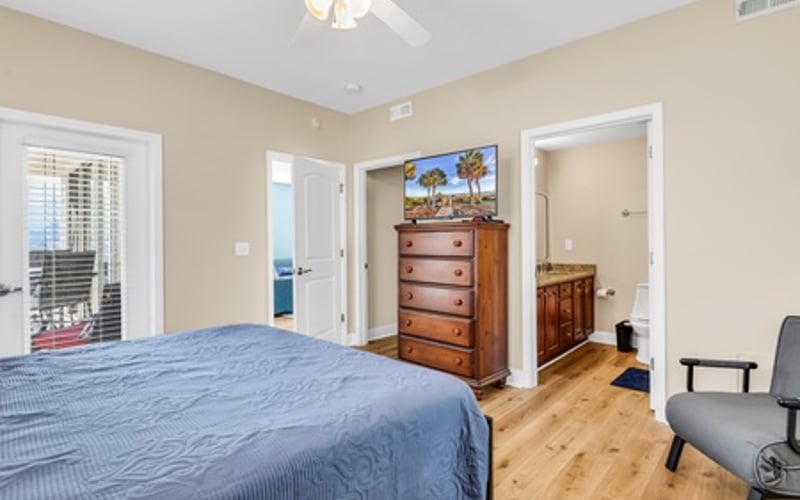 Master bedroom with blue bedding, wooden dresser, ceiling fan, and balcony access