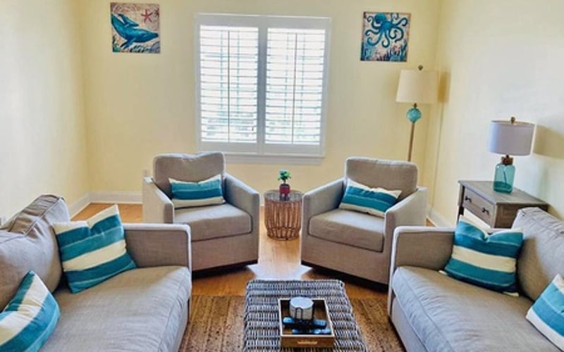 Bedroom with two twin beds, two gray armchairs, shuttered windows, and teal and white striped pillows throughout