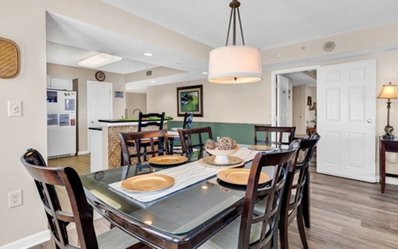 Dining room with dark wood table, four chairs, and pendant light fixture overlooking open kitchen