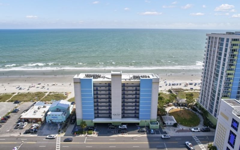 Beachfront hotel with blue and white facade overlooking sandy beach and ocean with gentle waves