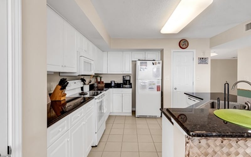 Galley kitchen with white cabinetry, stainless steel refrigerator, and tile flooring