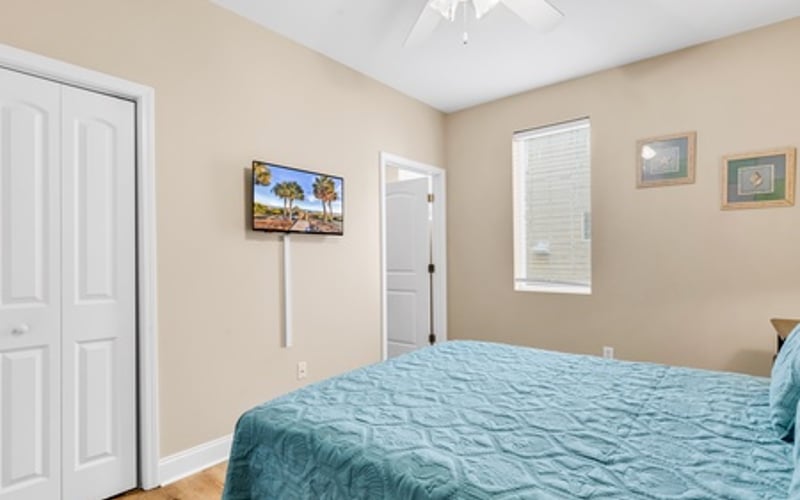 Bedroom with queen bed, blue bedding, beige walls, white ceiling fan, and hardwood flooring