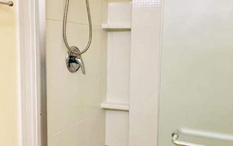 Shower stall with chrome showerhead and built-in shelf niche in cream-colored tile