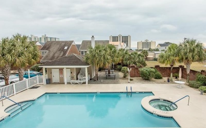Resort swimming pool with hot tub, pool house, and coastal town skyline in background