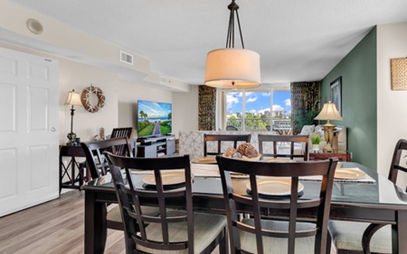 Dining room with black table and chairs, pendant light, city skyline view through windows, green accent wall