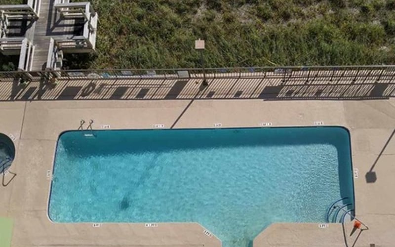 Overhead view of rectangular swimming pool with turquoise water, surrounded by concrete deck and forested area