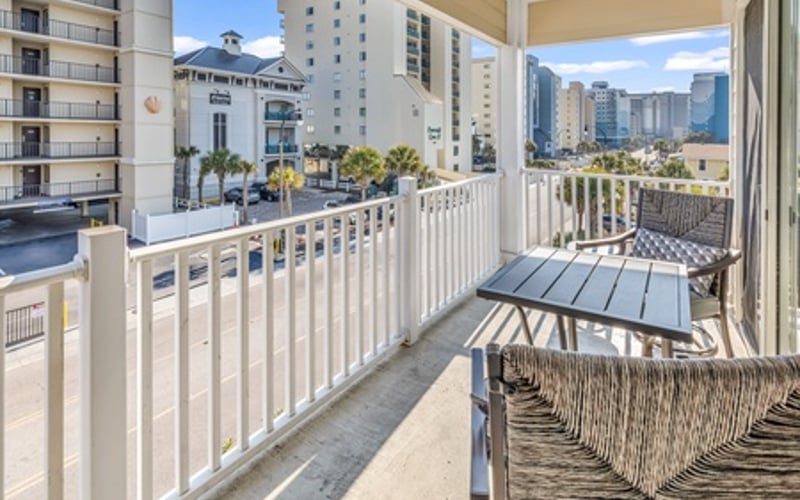 Balcony with white railing, lounge chairs, and city skyline view surrounded by high-rise buildings