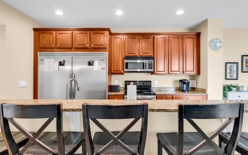 Kitchen with wood cabinetry, stainless steel appliances, and granite countertop with three black chairs at island