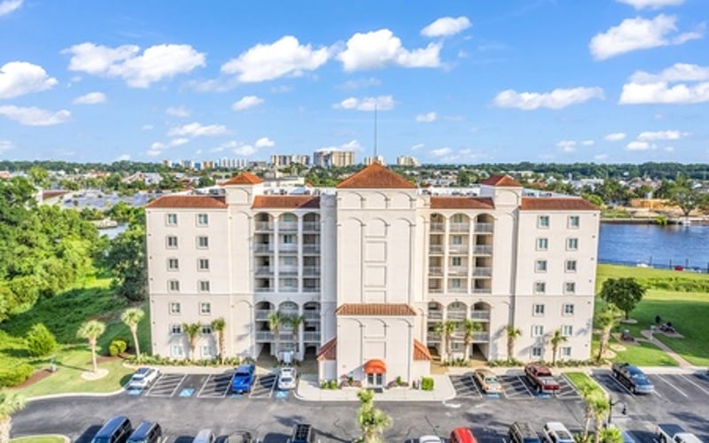 Aerial view of residential apartment building with parking lot and waterfront in background