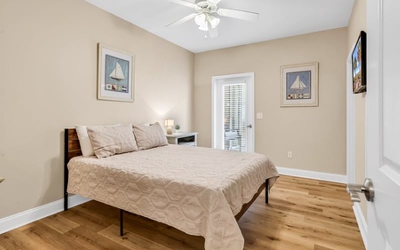 Bedroom with queen bed, ceiling fan, beige walls, hardwood floors, and glass door to patio