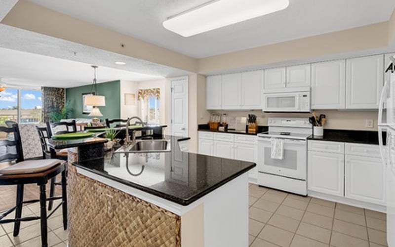 Open-plan kitchen with white cabinetry, black countertop island, and dining area with green accent wall