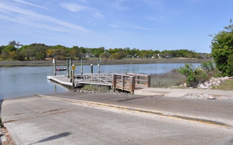 Concrete boat ramp leading to wooden dock on calm river with tree-lined banks
