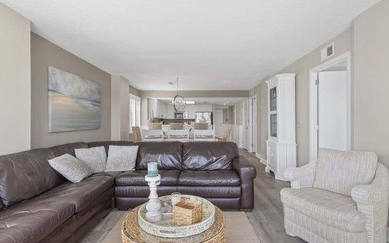 Open-plan living room with brown leather sectional sofa, woven round coffee table, and cream armchair