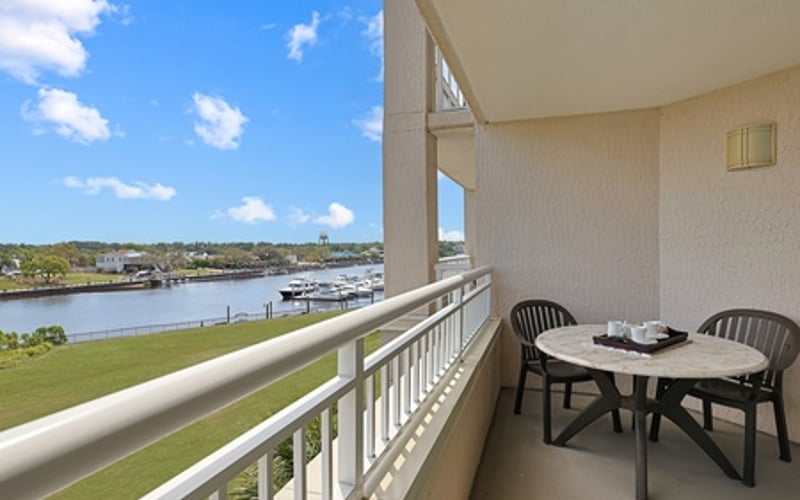 Balcony with dining table and chairs overlooking river, marina, and green lawn