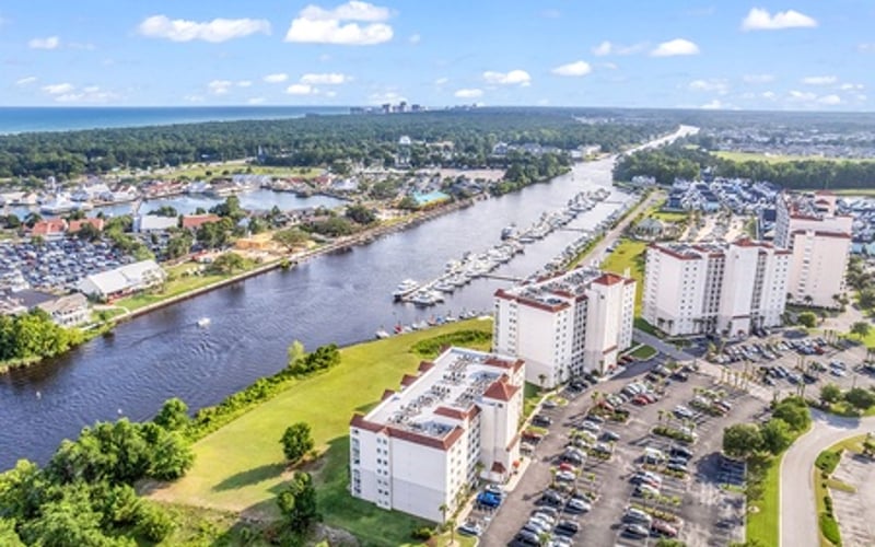Aerial view of riverside town with apartment buildings, parking lots, and moored boats along waterway