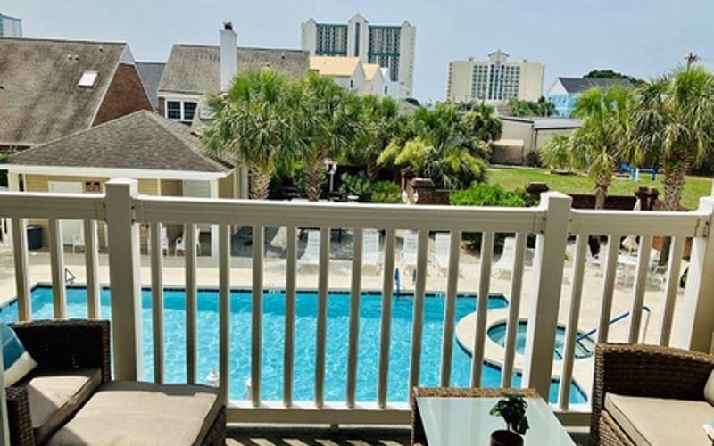 Deck with white railing overlooking swimming pool, palm trees, and coastal buildings
