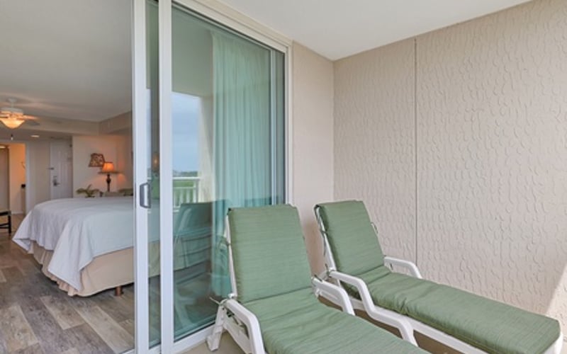 Balcony with two green lounge chairs overlooking bedroom with sliding glass doors