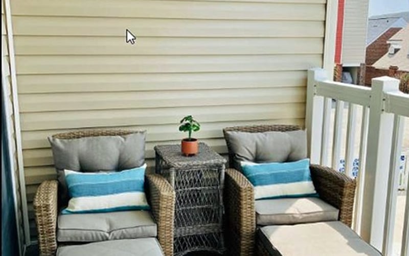 Wicker patio seating with blue and gray cushions, small side table, and footstools on a deck