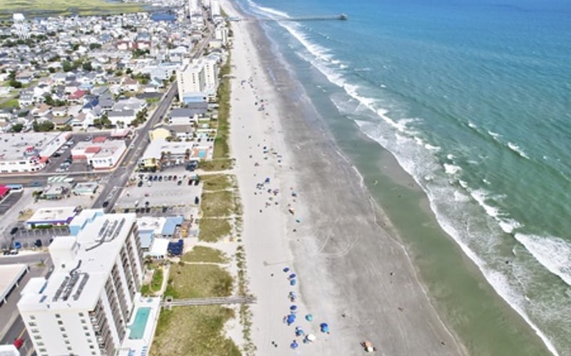 Aerial view of beachfront town with sandy beach, ocean waves, and residential buildings along the shore