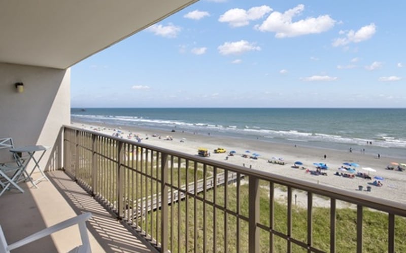 Oceanfront balcony with metal railing overlooking sandy beach and Atlantic Ocean with beach umbrellas
