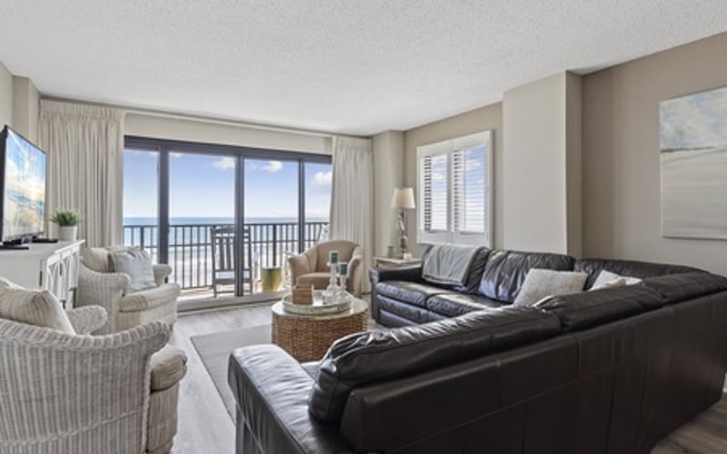 Spacious living room with black leather sofa, striped armchairs, and ocean view from balcony doors